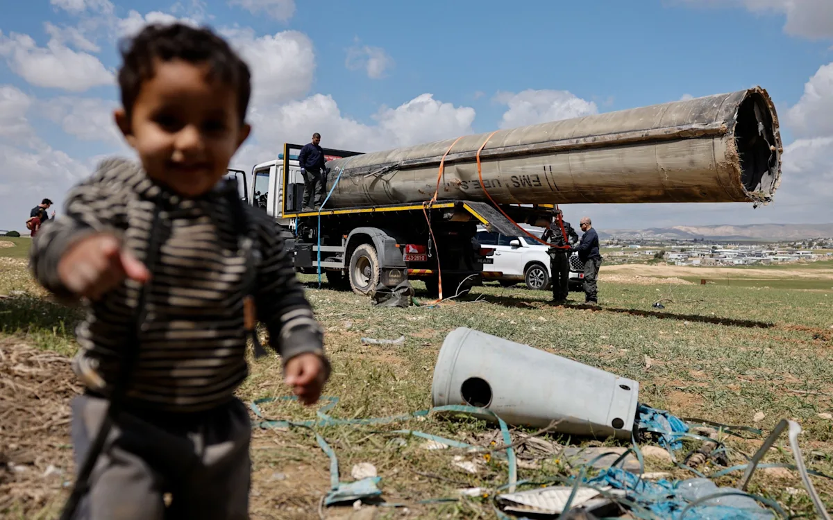 Aerial view of Iran's missile launchers, with a focus on the primary keyword phrase 'Iran missile launchers', the image depicts the launchers in a desert landscape, with a few buildings and roads in the background, the colour of the launchers is a mix of brown and green, allowing them to blend in with the surrounding environment, the image is a descriptive alternative text for the featured image