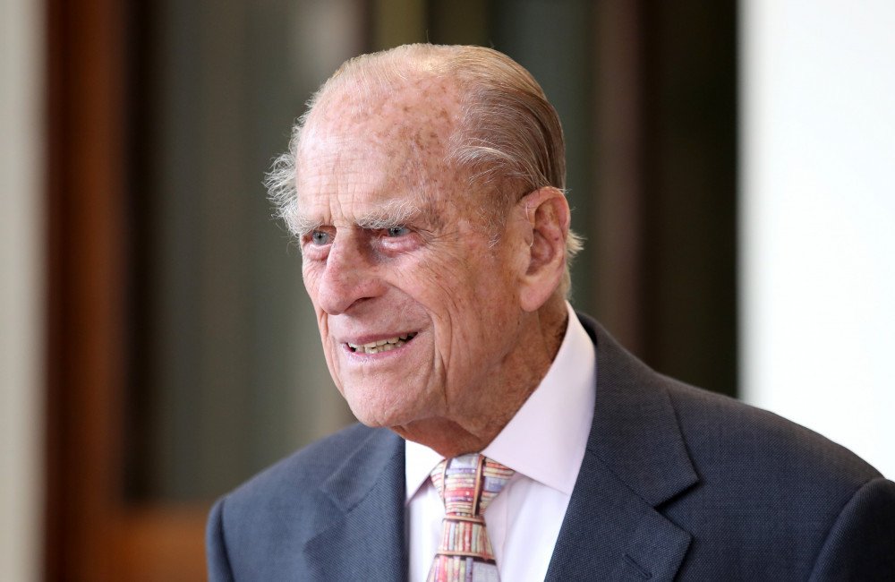 A photo of Prince Philip, the late Duke of Edinburgh, with a subtle background image of a hospital or medical equipment, symbolising his courageous fight against pancreatic cancer, with a caption that reads 'Prince Philip's Secret Battle'