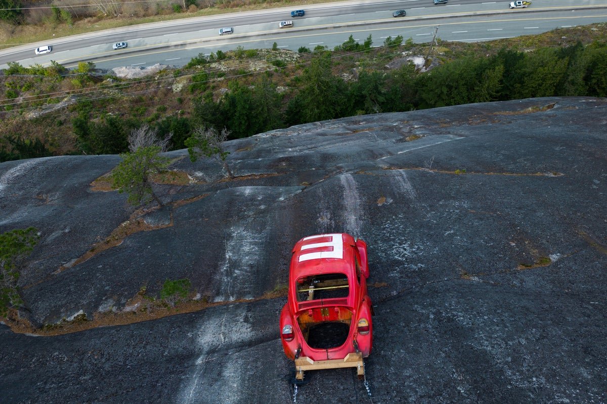 A car precariously perched on a rock face, with authorities warning the public to stay away due to the potential danger of the car prank