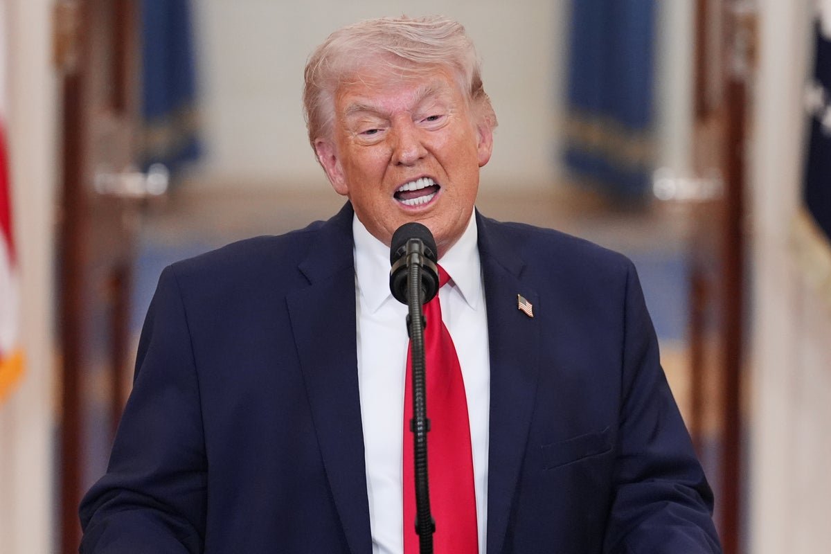 Donald Trump speaking at a rally, surrounded by supporters with MAGA hats, a mixture of colourful flags and banners on display, as he verbally attacks his former allies