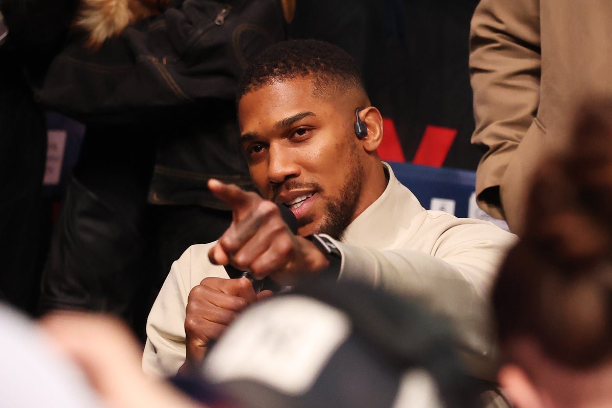 Anthony Joshua in the boxing ring, focusing on his training and ignoring the distractions, with a crowd of fans cheering him on, highlighting his commitment to the sport of boxing and his ability to handle pressure