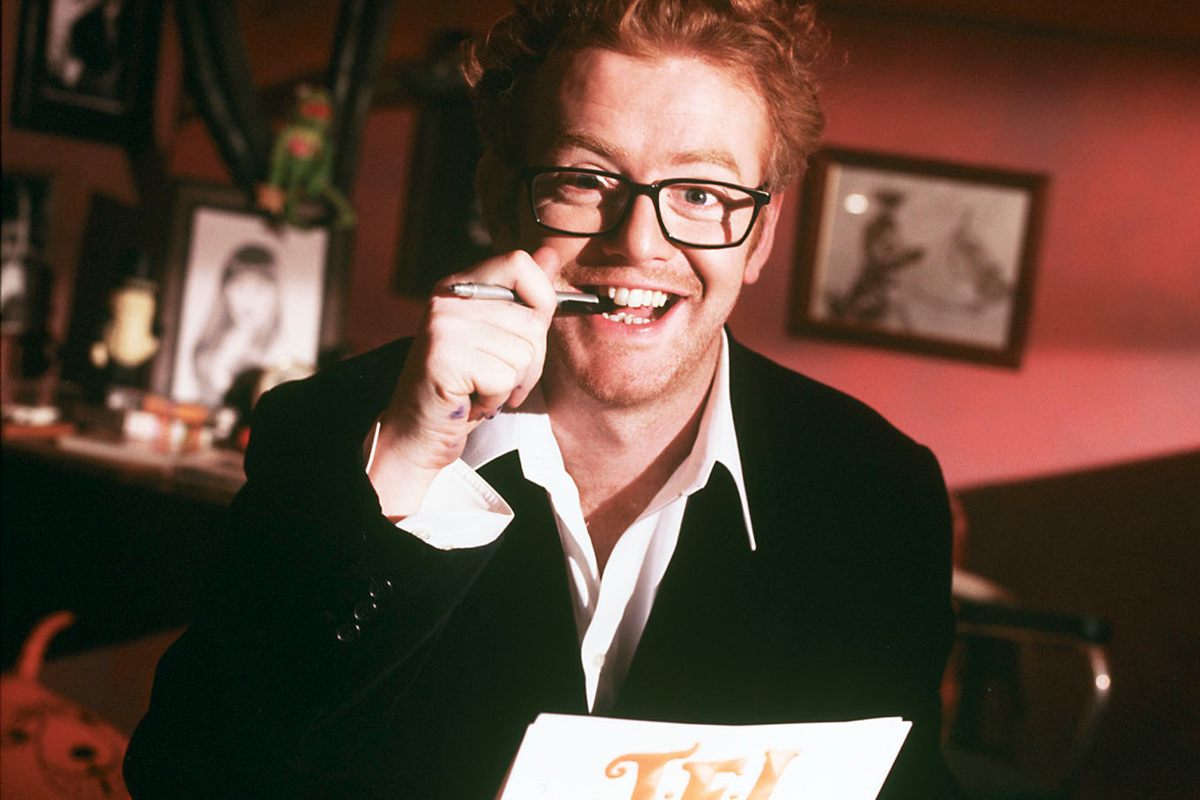 Chris Evans standing on stage, surrounded by a live audience, with a microphone in hand, ready to host the revamped TFI Friday show on Channel 4, bringing back nostalgic memories of the original series