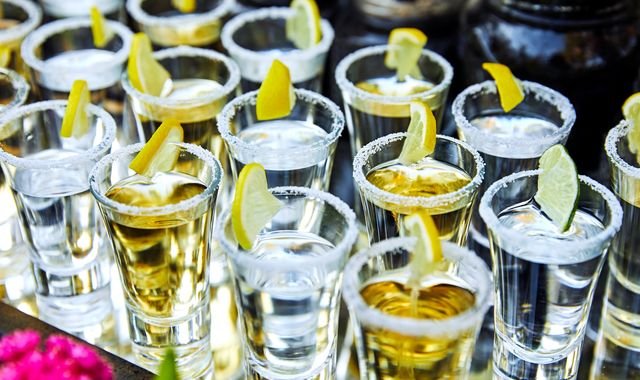 A woman holding a tequila shot on a cruise ship, with a blurred background of a bar and other passengers, highlighting the risks of excessive alcohol consumption on cruise ships, particularly with drinks like tequila