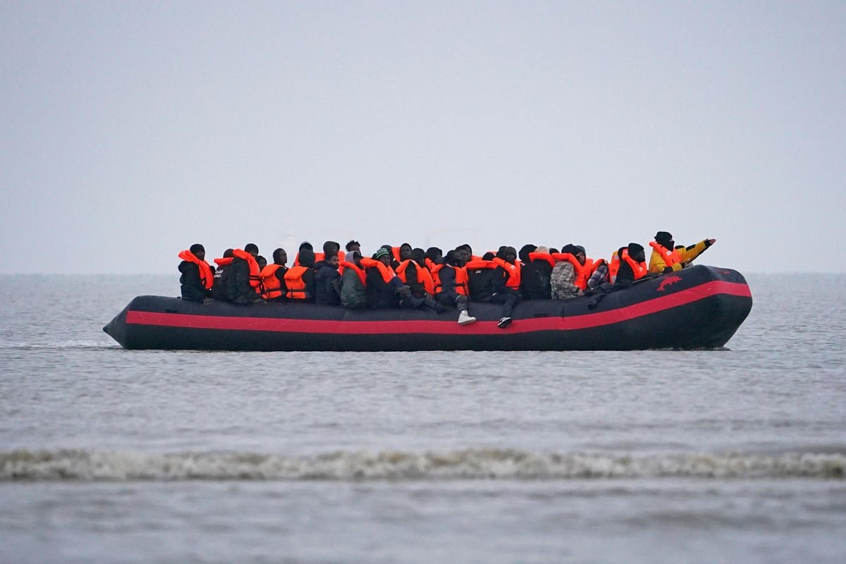 A crowded dinghy crossing the English Channel, with the UK coastline in the background, highlighting the risks and challenges associated with Channel crossings and the importance of safety and security