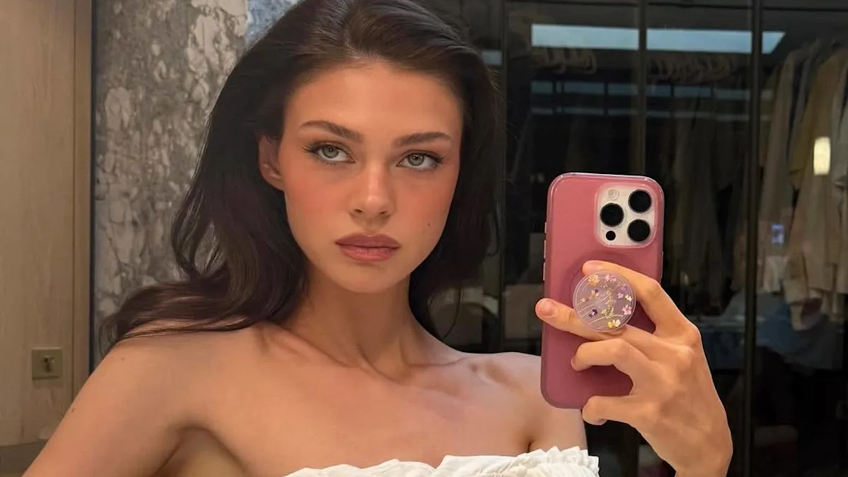 Nicola Peltz smiling and posing for a photo, with a subtle background colour, amidst her ongoing transformation and social media scrutiny