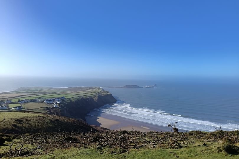 A dramatic photo of a coast guard rescue at Gower beach, with the incoming tide and a man being rescued in the distance, showcasing the power of the sea and the importance of coastal safety