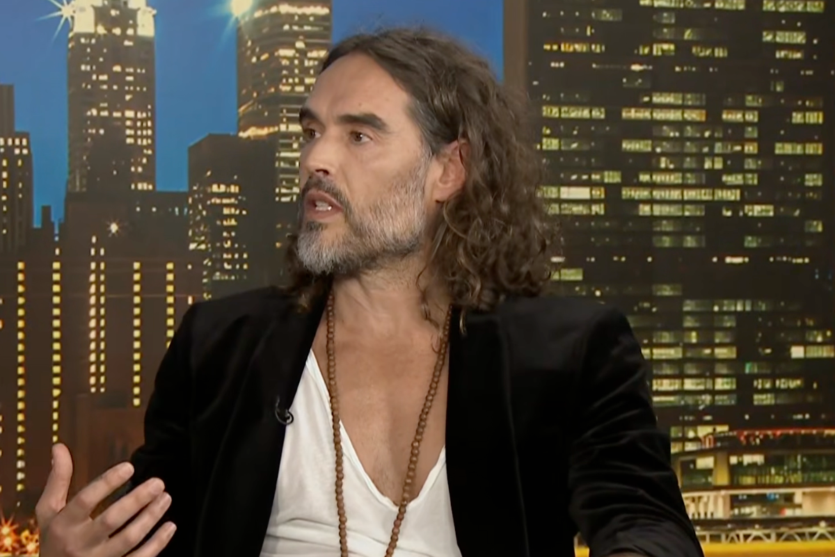 Russell Brand looking frustrated during his interview with Piers Morgan, as he struggles to find a Bible passage, with a colourful background and a mix of serious and humorous expressions