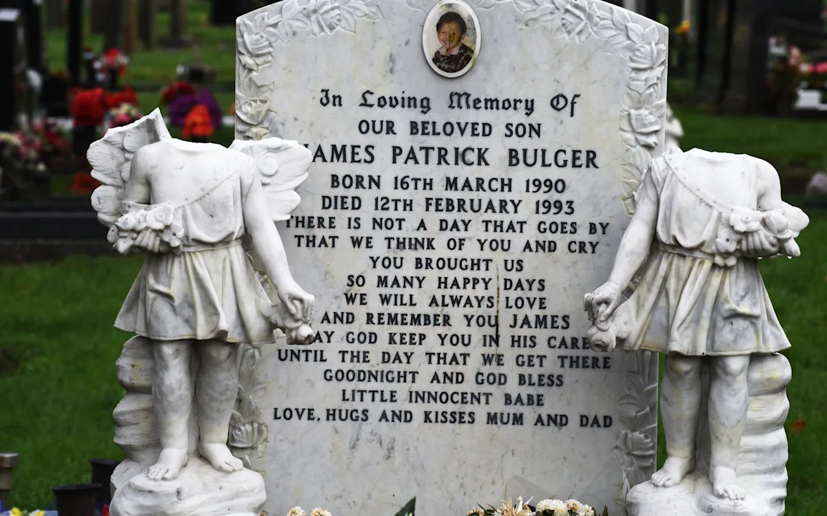 A photograph of a graveside, with flowers and tributes laid out in memory of James Bulger, a young boy who was tragically murdered in 1993, with a focus on the importance of respecting the dead and protecting graves and memorials from vandalism