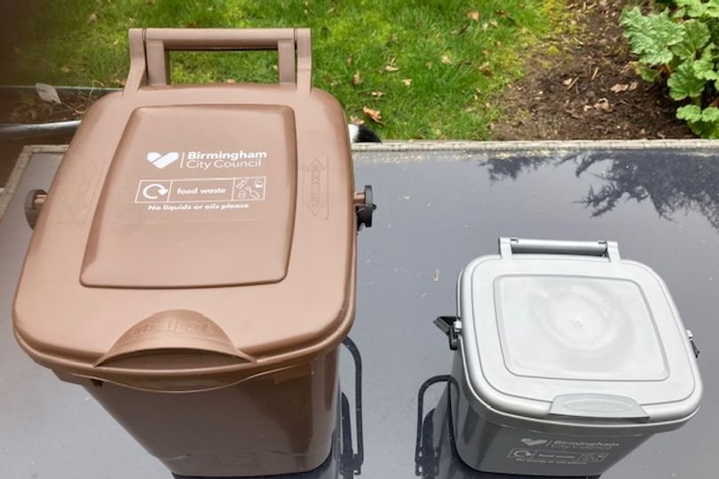A binman holding a food waste caddy with a red cross over a plastic bag, highlighting the importance of correct disposal and the primary keyword phrase food waste