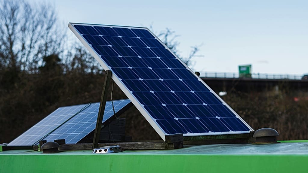 A person holding a plug-in solar panel, with a fridge and slow cooker in the background, showcasing the potential of solar energy to power everyday appliances