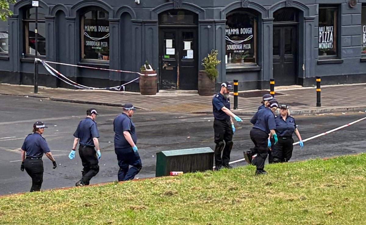 A descriptive image of a London street with a police cordon in place, with people gathered behind the tape, after a drive-by shooting in Brixton, with a focus on the Brixton shooting