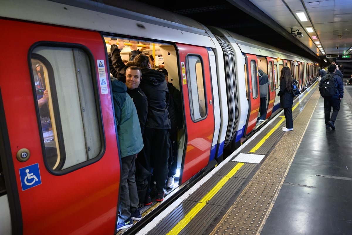 A crowded London tube platform with a sign reading 'strike action' and a union representative speaking to a crowd of commuters, highlighting the primary keyword 'tube strikes'