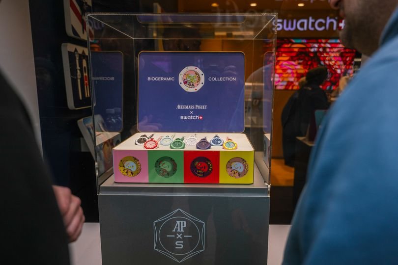 A huge crowd of people waiting outside a Swatch store in London, eager to purchase the new watch, with a focus on the latest timepiece and its unique design and colour