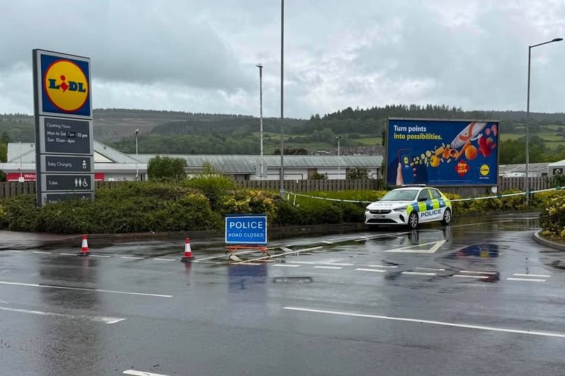 A sombre and deserted seaside town street with a supermarket in the background, as the community mourns the death of a man who died outside the store, with a focus on the tragic incident and its impact on the town