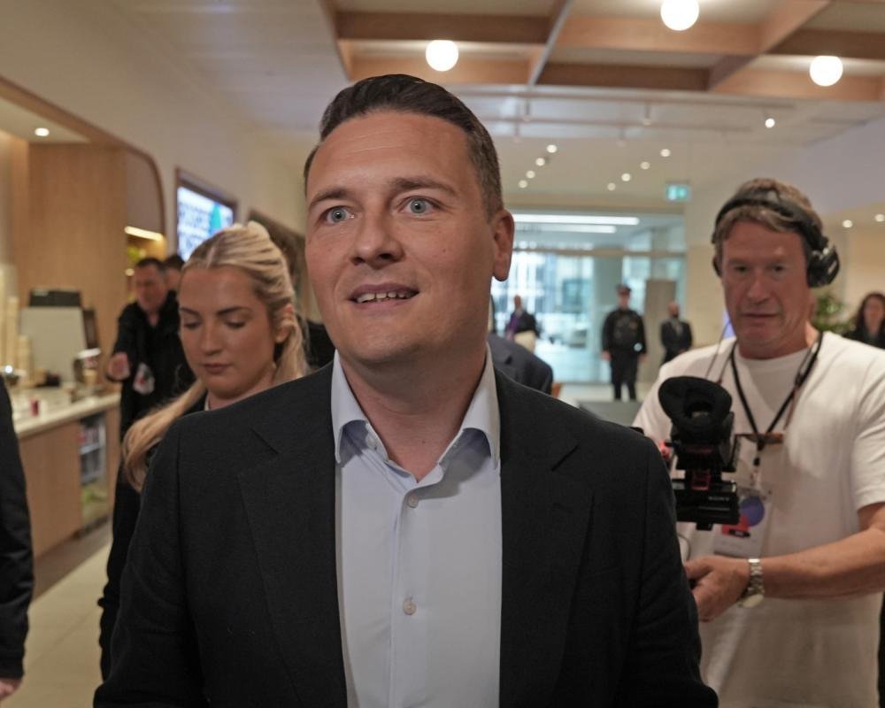 Wes Streeting speaking in parliament, calling for the UK to rejoin the EU, with a backdrop of EU flags, amidst a complex and uncertain future for the UK and EU relationship, with the Labour party's leadership under scrutiny