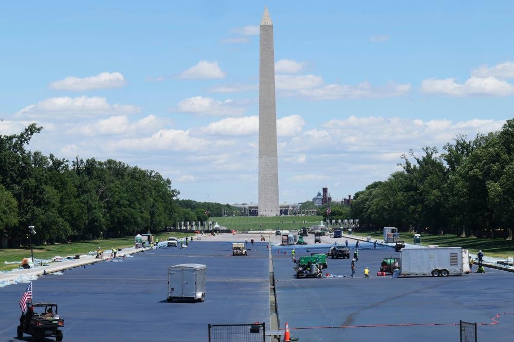 Workers in high-visibility vests and hard hats surrounded by construction equipment and materials, with a blue reflecting pool in the background, as they rush to meet the deadline for Trump's makeover project, highlighting the importance of worker safety and wellbeing