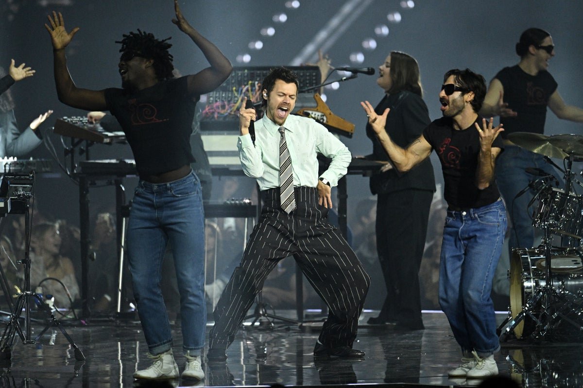 Harry Styles performing on stage with a large crowd of fans in the background, with a focus on the stage design and fan experience