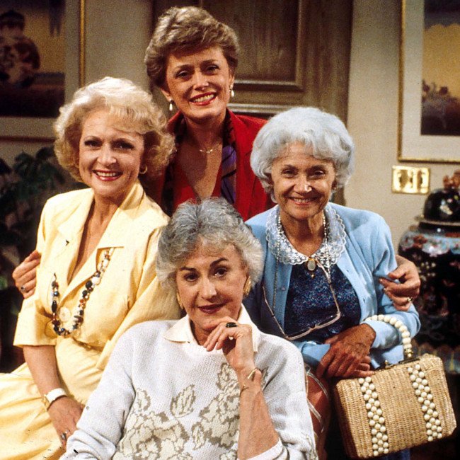 A group of older women sitting on a couch, laughing and chatting, with a warm and colourful background, showcasing the iconic characters of Golden Girls and the potential of a modern remake
