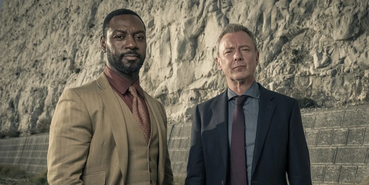 A detective standing in front of a crime scene, with a puzzled expression, analysing the clues and trying to unravel the mystery of the latest case, with a cityscape in the background, showcasing the show's dark and gritty tone, with a touch of colour and humour, as the detective series returns to ITV