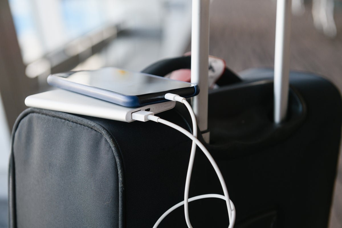 A passenger holding a portable charger on a flight, with a laptop and phone charging in the background, highlighting the importance of understanding airline rules and regulations for portable chargers