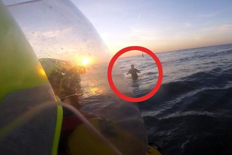 A woman trapped in sinking sand on a North Wales beach, with rescuers working to free her as the tide rises, demonstrating the importance of beach safety and emergency response