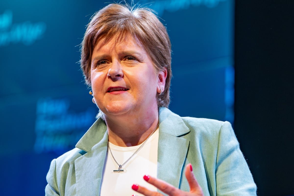 Nicola Sturgeon, the former First Minister of Scotland, stands outside a London building, surrounded by media, as she defends her record amidst controversy surrounding her husband's conviction, with a mix of curiosity and scrutiny from the public