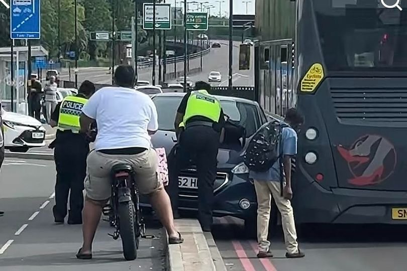 A car stuck facing the wrong way beside a bus on a busy Birmingham route, with people gathered around, looking concerned and amused, highlighting the importance of road safety and cautious driving, with the primary keyword being Birmingham bus route