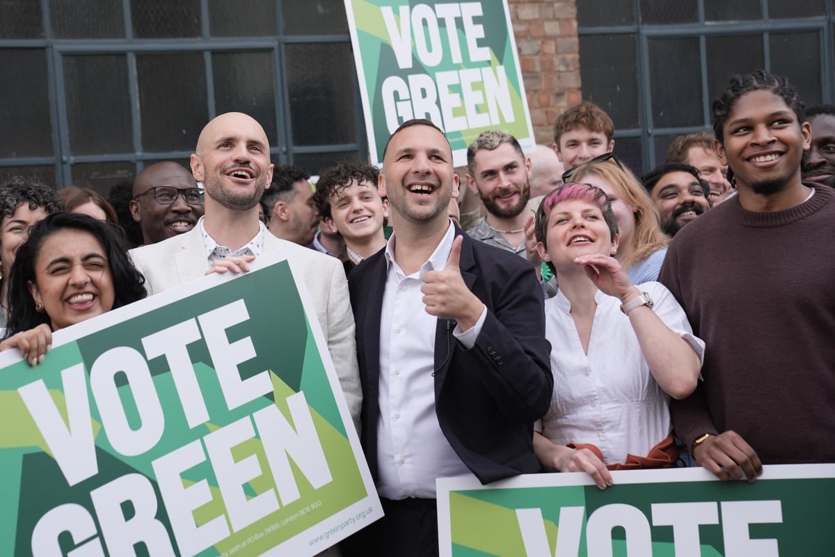 Green Party members celebrating the reversal of the Gaza ban in a London town hall, a significant development in the party's history and a testament to its commitment to social justice and human rights, with a focus on environmental issues and community wellbeing
