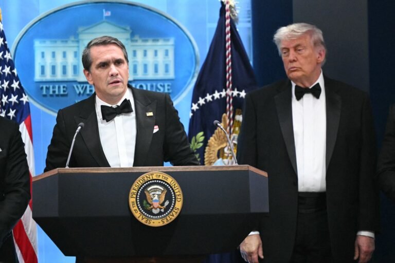 Acting AG Todd Blanche speaking at a press conference about Trump's potential prison sentence, with a serious expression and a backdrop of American flags, analysing the behaviour of the former President