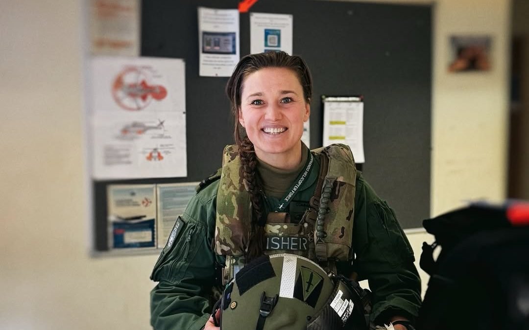 A photo of a female commando in uniform, with a helicopter in the background, symbolizing the UK's only female commando who was a victim of a recent helicopter crash, highlighting the importance of women in the military and the risks they face