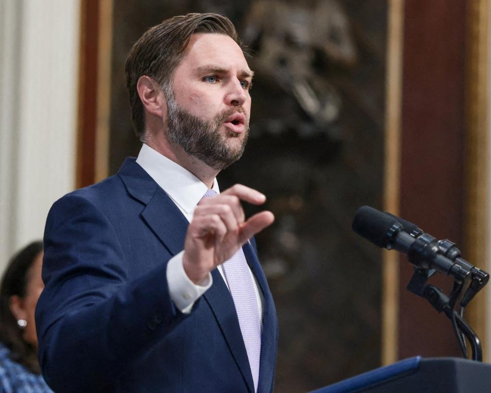 A photo of JD Vance speaking at a rally, with a crowd of people in the background, with a caption that reads 'JD Vance sparks outrage with migrant invasion claims', highlighting the controversy surrounding his comments on migrant invasion and immigration reform