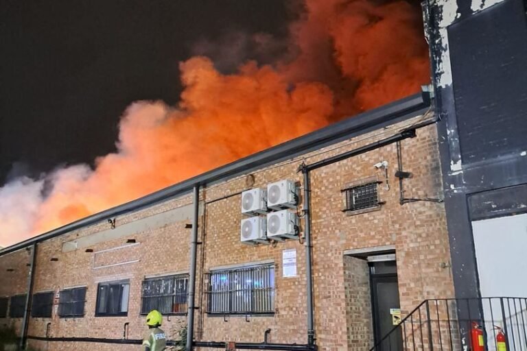 A dramatic image of a fire in a residential area, with flames engulfing a building and emergency services responding to the incident, highlighting the importance of fire safety and emergency response in the community, particularly in relation to the Brent fire
