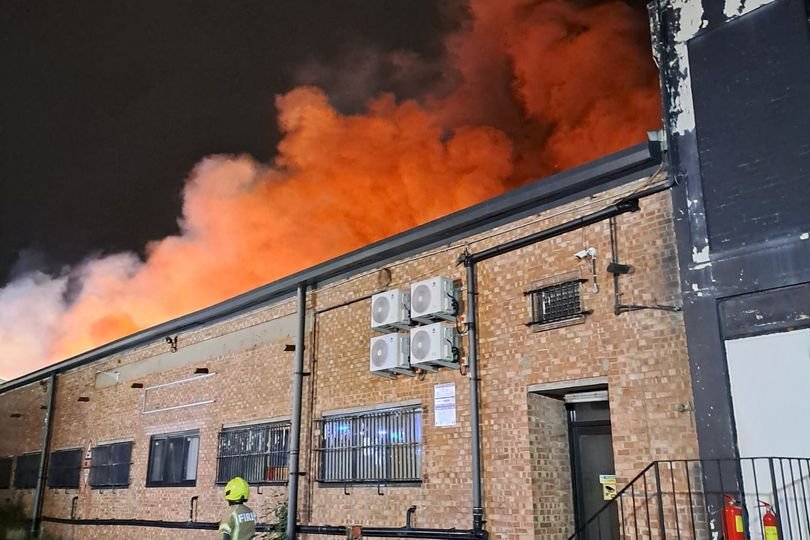 A dramatic image of a fire in a residential area, with flames engulfing a building and emergency services responding to the incident, highlighting the importance of fire safety and emergency response in the community, particularly in relation to the Brent fire