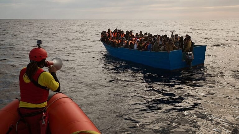 A group of migrants standing together, looking out at the sea, with a European Union flag waving in the background, symbolising the EU migration pact and the complex issues surrounding asylum and migration