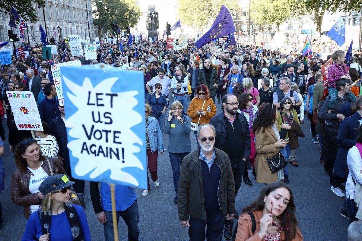 A crowd of protesters holding signs that read 'Second Referendum Now' and 'Reform Brexit' outside the Houses of Parliament in London, with a blue sky and fluffy white clouds in the background, symbolising the ongoing demand for a second Brexit referendum and the UK's uncertain future