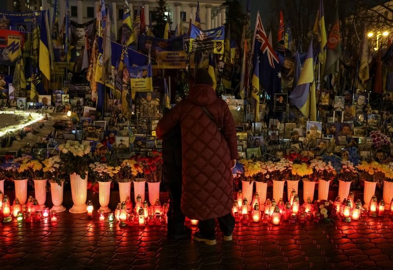 A young woman in a military uniform, with a solemn expression, standing in front of a Ukrainian flag, symbolising the conflict between Ukraine and Russia, with a focus on the recruitment of young women to target Ukrainian servicemen, highlighting the desperation of Russian forces and the need for international intervention