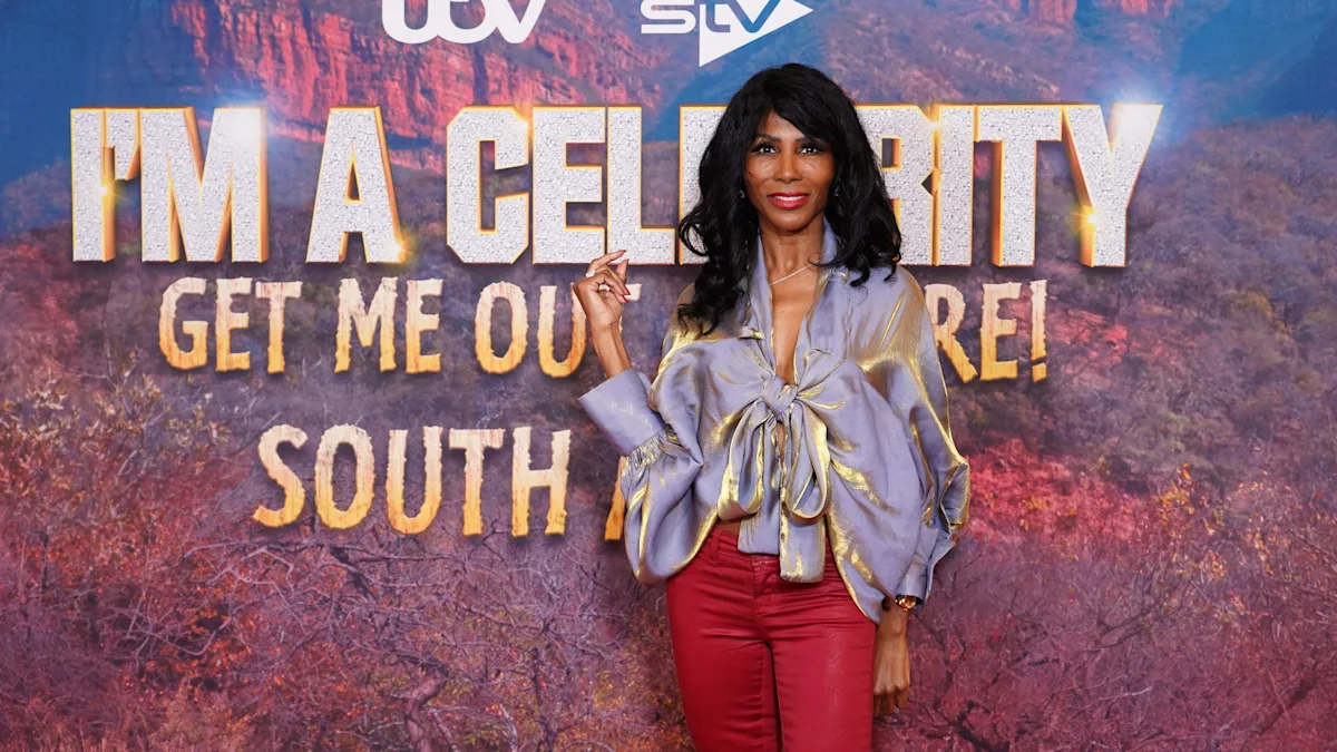 Sinitta standing in front of the I'm a Celebrity... South Africa logo, looking excited and a bit shaken, with a mix of colour and emotion on her face, reflecting on her time in the jungle