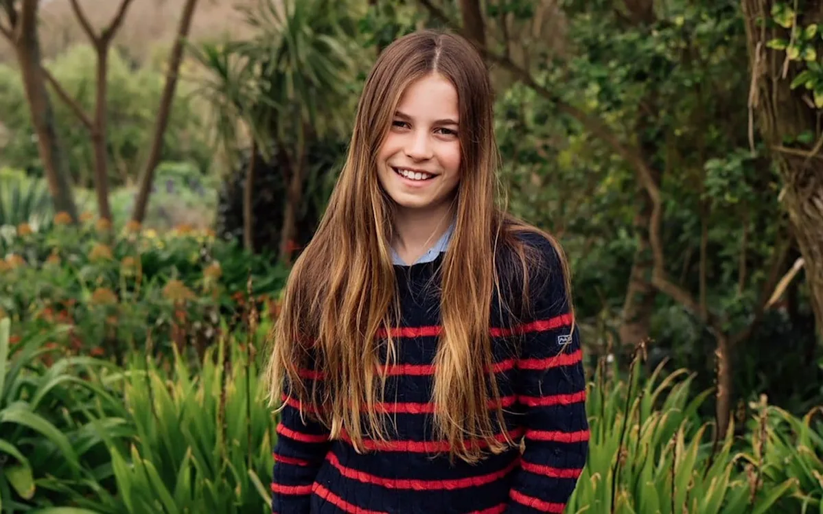 Princess Charlotte smiling and happy in her 11th birthday portrait, wearing a bright coloured dress and standing in a beautiful outdoor setting, surrounded by nature and filled with joy, the photo captures her lively personality and striking resemblance to her mother Kate Middleton