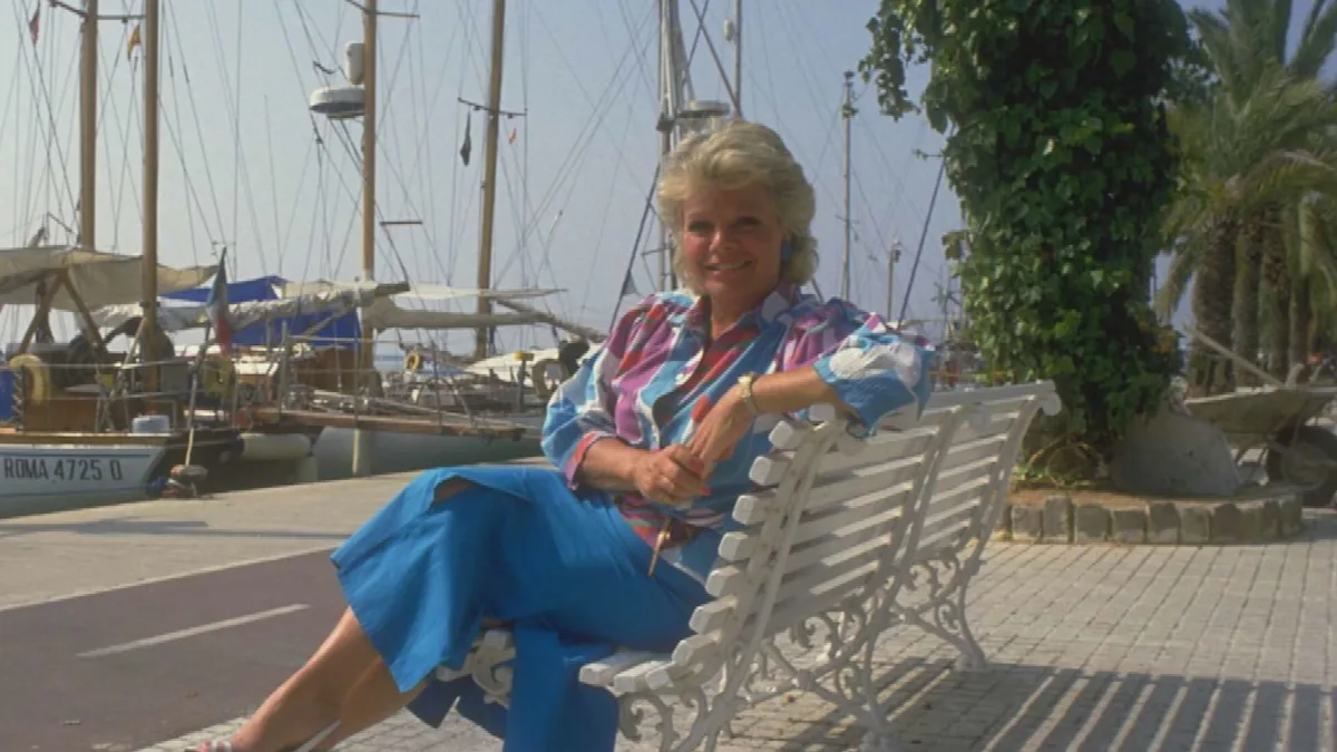 Judith Chalmers, renowned TV presenter, standing in front of a colourful backdrop, with a warm and welcoming smile, showcasing her love for travel and exploration, a true legend in the world of television