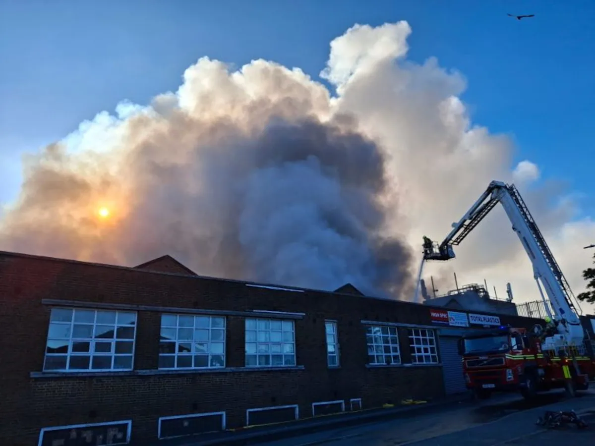 A large fire on an industrial estate, with flames engulfing a warehouse and firefighters battling to contain the blaze, highlighting the importance of fire safety and prevention measures
