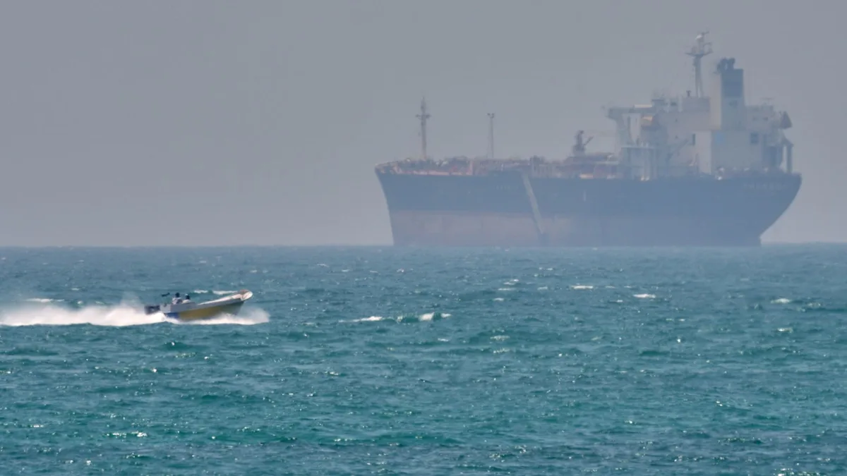 Aerial view of a commercial ship in the Strait of Hormuz, with the Iranian coastline in the background, highlighting the primary keyword phrase Iran blockade and the context of the US strike