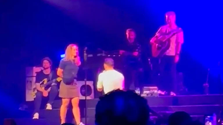 A man proposing to his girlfriend on stage in front of a large crowd, with a mix of shocked and amused expressions on the faces of the audience members, highlighting the unpredictability of public proposals and the importance of being mindful of the other person's boundaries and feelings