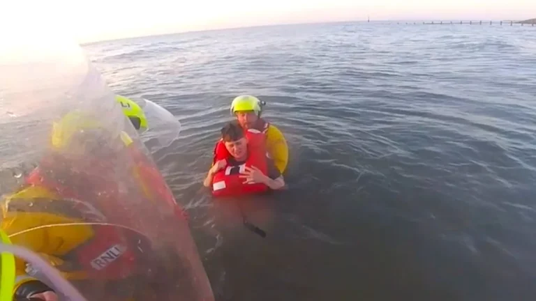 A descriptive image of RNLI rescuers helping a woman stuck in quicksand on the Welsh coast, with the tide approaching, highlighting the primary keyword of quicksand rescue