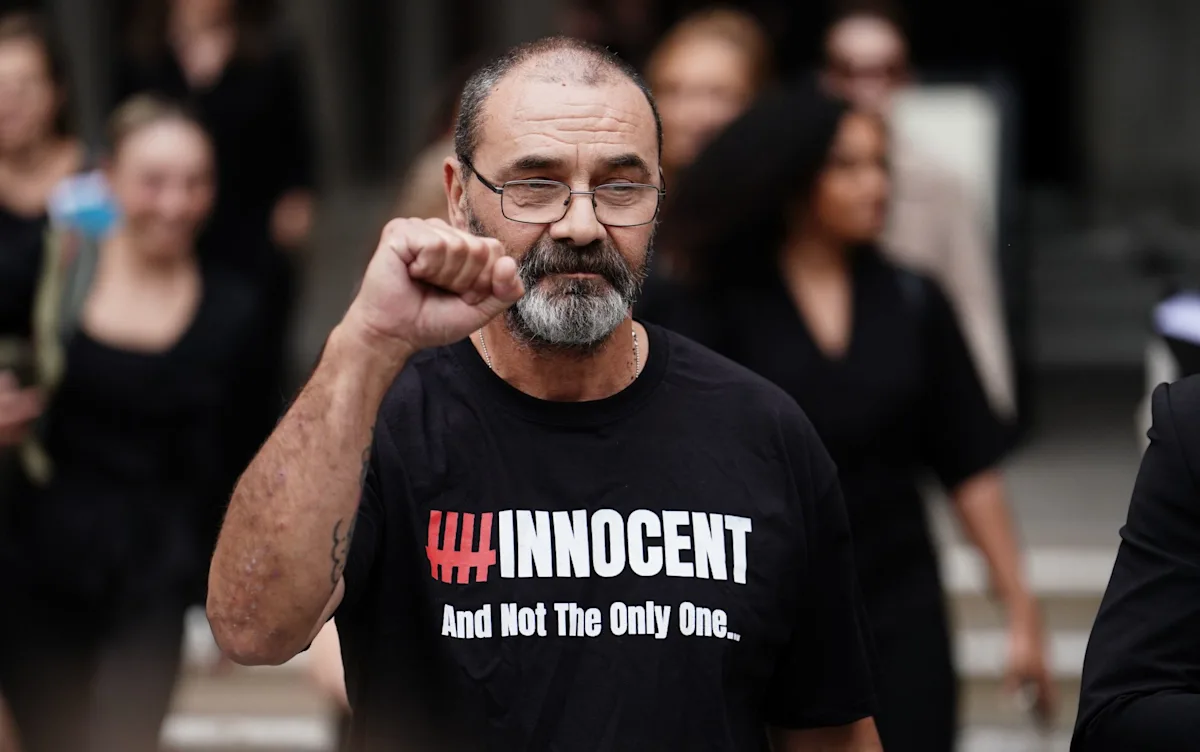 A man holding a sign that reads justice for all, with a blurred background of a court room, the primary keyword justice system is highlighted in this image