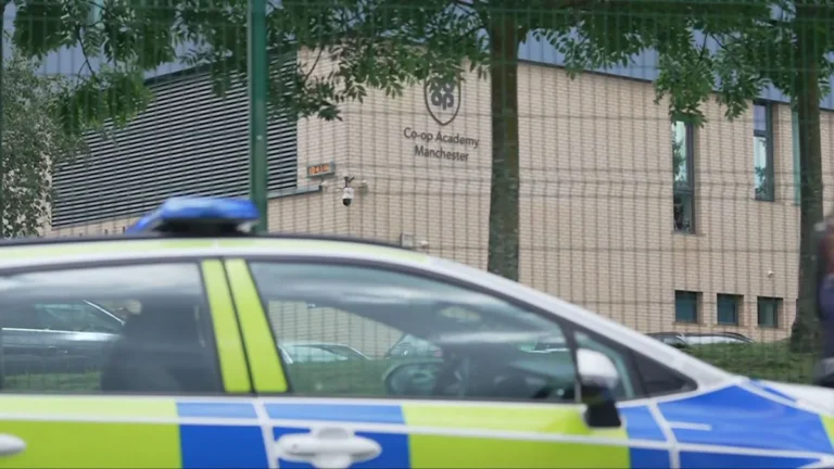 A photo of a school in Manchester, with a police car and ambulance outside, following a stabbing incident that left two pupils and a teacher injured, highlighting the need for increased school safety measures and support for the victims and their families