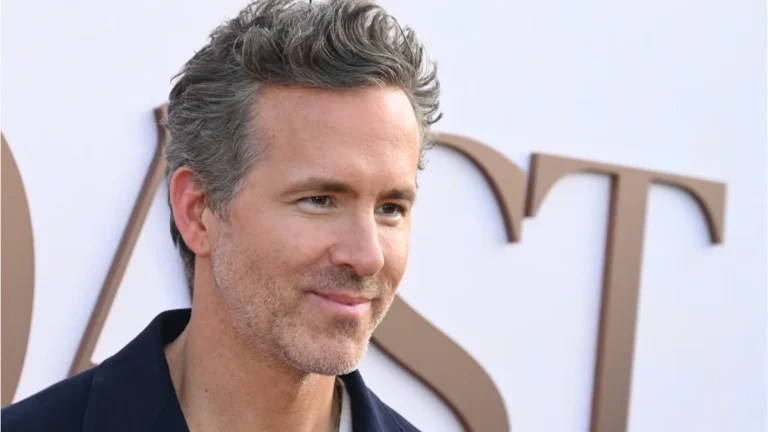 Ryan Reynolds, a Canadian actor, standing on the red carpet with a charming smile, his left side fully recovered from the car accident 30 years ago, a true testament to his strength and perseverance, with a crowd of fans and photographers in the background