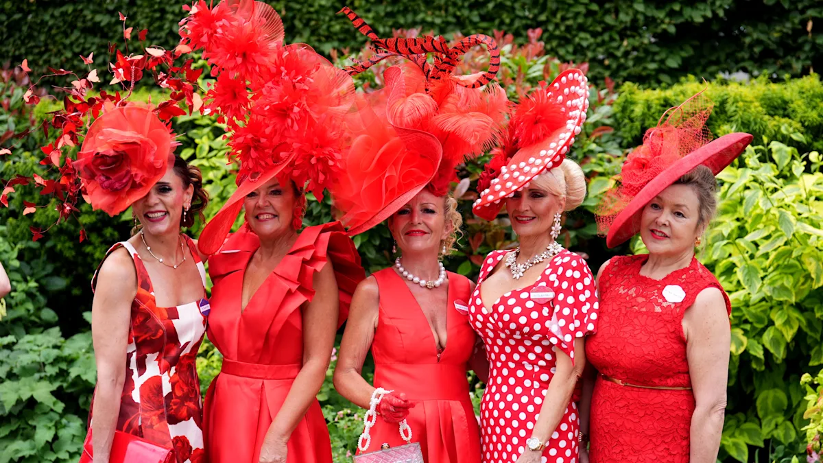 A woman wearing a vibrant pink hat with feathers and flowers, surrounded by a crowd of people at Royal Ascot, showcasing the event's unique and creative hats